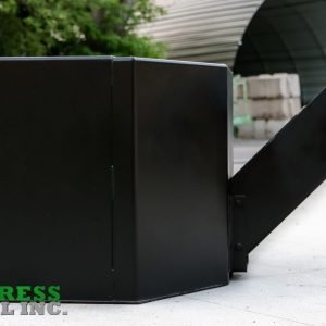 An Express Steel Manual Concrete Placement Bucket, a large black metal industrial attachment with a side chute, sits on outdoor concrete near a road. The green and gray Express Steel Inc. logo is in the bottom left corner.