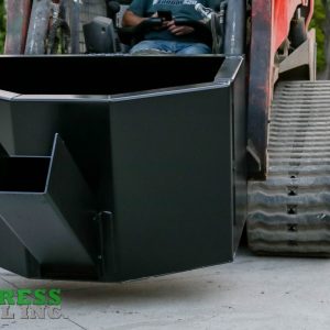 A close-up of an Express Steel Manual Concrete Placement Bucket, finished in black steel and mounted on a skid steer loader. The “Express Steel Inc” logo appears in the lower left. The machine is outdoors on concrete near trees and a building.