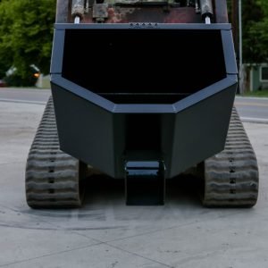 An Express Steel Manual Concrete Placement Bucket in black is attached to a tracked vehicle, facing the camera outdoors by a road. The Express Steel Inc. logo appears in the lower left corner of the image.