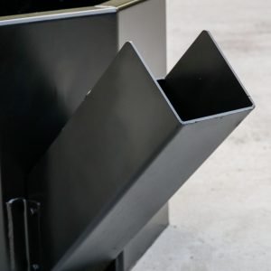A close-up of an Express Steel Manual Concrete Placement Bucket, featuring a black metal body with an angled chute on its side, sits on a concrete surface. The EXPRESS STEEL INC. logo appears in the bottom left corner.