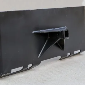 The Express Steel Hitch Plate is a black metal skid steer attachment featuring a central mounting bracket and rectangular tube receiver, shown standing upright on a light concrete surface.