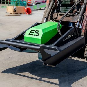 A close-up of an ES 60" Standard Brush Cutter (up to 60HP), green and black, mounted on the front of a tracked skid steer loader, positioned outdoors on a concrete surface.